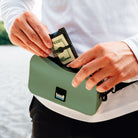 Person using a green waterproof pouch by a body of water